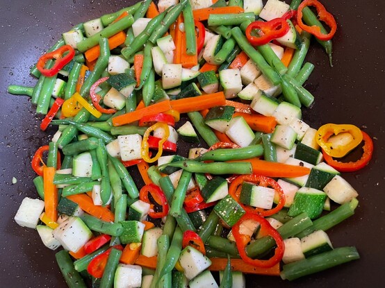 A vegetable stir-fry in pan with French green beans, chopped zucchini, sliced baby bells, carrot slivers, salt and pepper.