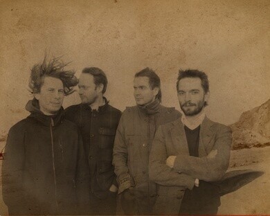 Foto von Mitgliedern der isländischen Band "Sigur Rós". Vier Männer mittleren Alters stehen zusammen. Das Bild ist in Sepia Schwarz/ Weiß gehalten.