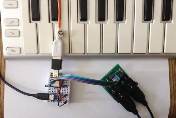 Photo of a Seeed Studio XIAO SAMD21 on a mini solderless breadboard connected to a Serial MIDI module and a USB MIDI controller keyboard.  The XIAO is powered independently via a micro USB cable.
