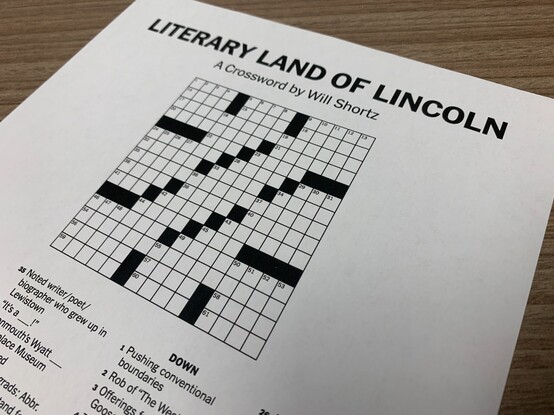 Closeup of a crossword puzzle with title "Literary Land of Lincoln" by Will Shortz. The image is at an angle and is not framed with the intention of the viewer being able to see many of the clues. One clue that is visible is "Noted writer / poet / biographer who grew up in Lewiston"