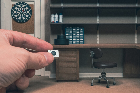Scale model of David's bedroom from the 1983 movie Wargames. A regular sized hand is holding a miniature speaker. A few other props can be seen, a dart board on the upper left, a chair on the lower right, amongst other things.
