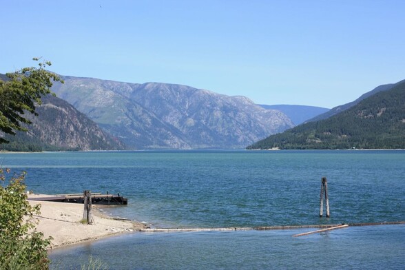 A lake surrounded by hills, a beach in the foreground. This is Arrow Lake, and we are looking toward the narrows that lead into the Upper Lake. 