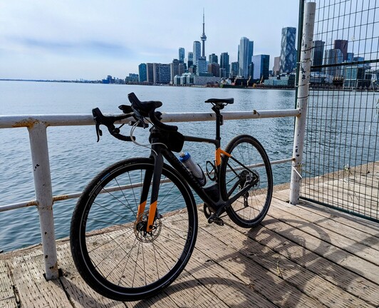 My bike leaning on a railing at polson pier with a skyline background of Toronto.