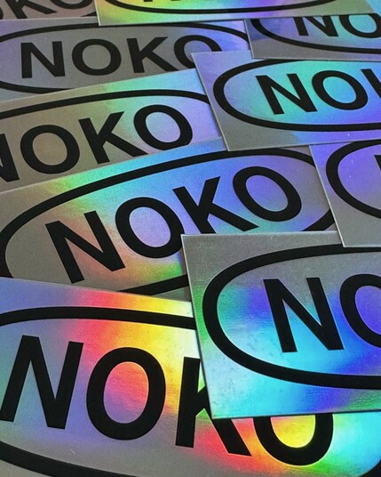 lots of silvery holographic stickers containing an oval shape with "noko" in it. up-close view.
