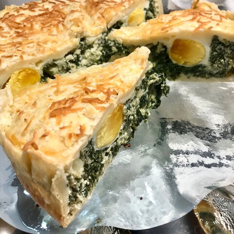 A close-up view of a slice of the torta, showing crust on top and the center which is filled with spinach and ricotta. A cooked egg, sliced in half is in the center of each piece of pie.  The pie is sitting on a clear glass plate. 