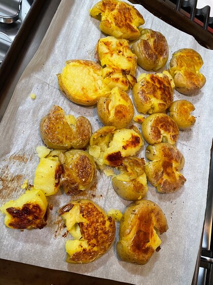 A sheet pan covered in parchment paper with roasted, smashed, Yukon gold potatoes.
