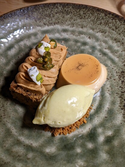 A dessert made of coffee panna cota, a pistacho ice cream and a crumble cake on the side.
