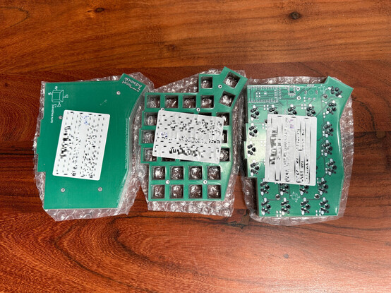 Three stacks of plastic wrapped, green PCBs for a split mechanical ergo keyboard called Sofle. On the left is the bottom plate, in the middle the top plate and on the right the actual PCB.