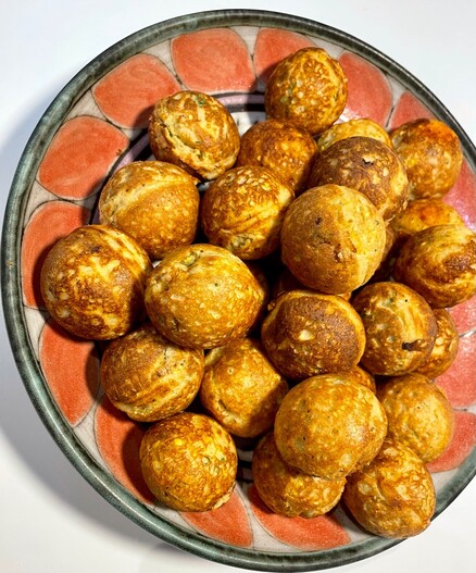 A round ceramic platter with coral tones. The platter is filled with round, cooked, savory ebelskiver treats. Not shown: the yogurt-herb dipping sauce.