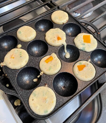 The batter is sitting in the ebelskiver pan. Small squares of cheddar have been dropped into the center of the batter, so that each one will have a cheesy center.