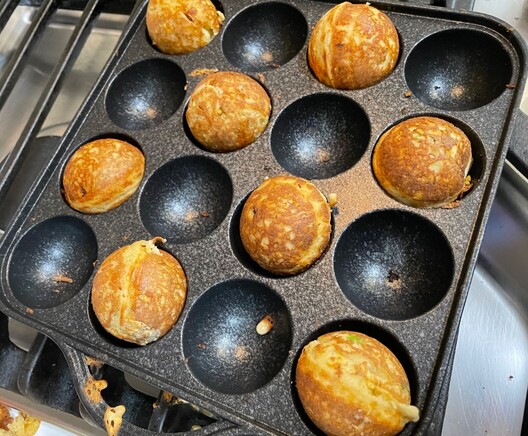 An ebelskiver pan with some cooked, savory treats. They are round and look like donut holes, but these are savory. 