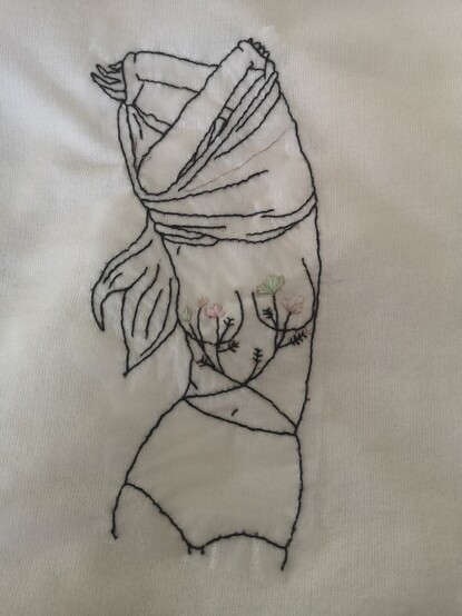 Broderie d'une femme se déshabillant avec des fleurs sur le torse. Les fleurs semblent trop claires par rapport au reste du dessin parce qu'elles sont pastels