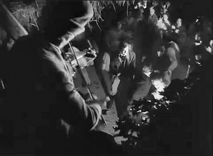 Walter Huston as the Devil playing the fiddle at a barn dance overlooking people dancing in the barn below