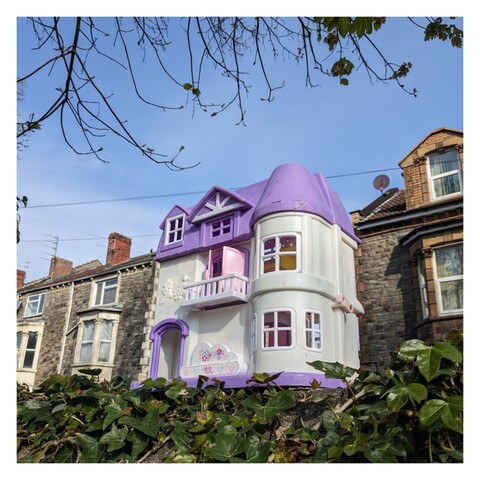 A plastic dolls house sitting on a wall, taken from an angle which makes it look as if it might be one of the houses on the street.