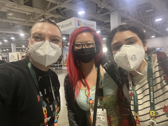 Three women taking a selfie in front of the PyCon US expo hall 