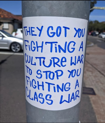 A handwritten poster, stuck to a traffic light somewhere in Australia saying “THEY GOT YOU FIGHTiNG A CULTURE WAR TO STOP YOU FIGHTING A CLASS WAR”.