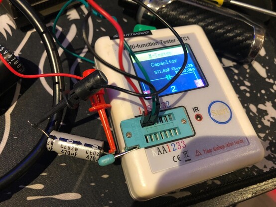 A photo of a multifunction electronic tester connected to a capacitor rated at 470 microfarads, measuring 571 microfarads on the device.