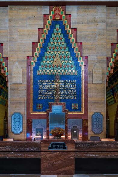 A photograph of the lobby of the Guardian Building featuring highly-geometric, Aztec design traits with a very vivid color palette. Above the front desk, there is a decorative design that reads "Founded on principles of faith and understating, this building is erected for the purpose of continuing and maintaining the ideals of financial services which promoted the organization of the institution." There is a smaller plaque mounted on the center of the front deck that reads "Guardian Building". The typeface is highly distinctive.