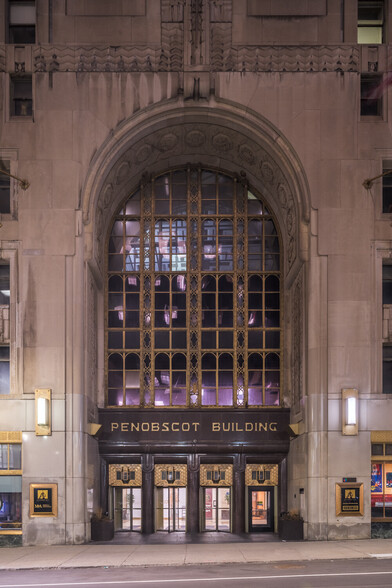 A photograph of the Penobscot Building entrance in Downtown Detroit taken from Griswold Street at dusk. The entrance features a large, domed, white stone entrance with gold trimmed glass panes taking up the top two-thirds of the entrance. The words "Penobscot Building" is featured just above the four doors that lead into the building. The typeface is similar to that found in the Guardian Building featuring sharp path deviations where the shapes would normally be smooth curves. However, it differs a bit as the corners of each letter seem less "sharp".