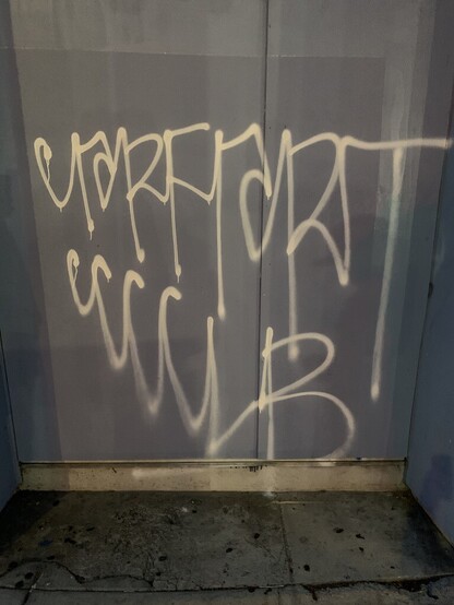 a photo of very messy graffiti on a wall. It's hard to read, but it looks like a form of cursive. Each word appears to get bigger as it goes from left to right. 