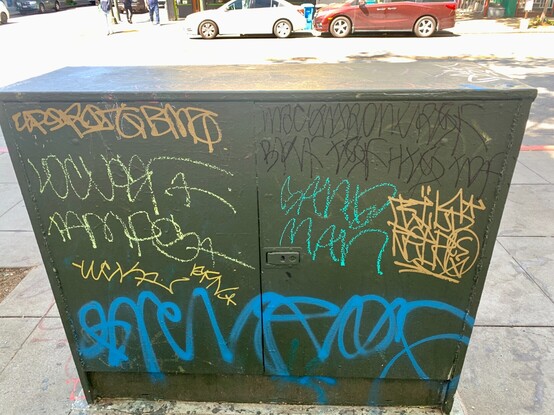 Some public architecture covered with multiple tags from graffiti artists. Different media is used, but the names all have a similar cursive style. 