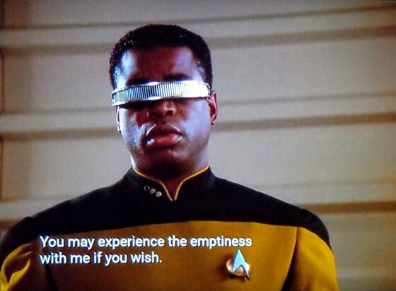 TNG scene, we're close in on Geordi La Forge, in gold starfleet uniform, with trademark eye visor on. He looks kind of depressed. Like visually he looks like the feeling you get when you eat the whole burrito instead of saving half for later. Closed caption reads, "You may experience the emptiness with me if you wish." 