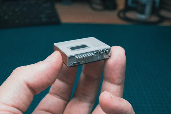 miniature 1:12 scale VCR held by a regular sized hand, over a green desk mat