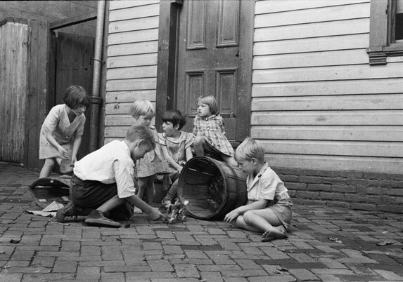 Carl Mydans photographed six young children playing on a brick sidewalk in front of a row house in the Georgetown section of Washington, D.C., in September 1935. In the black-and-white photo, they are using several bushel baskets in their play.