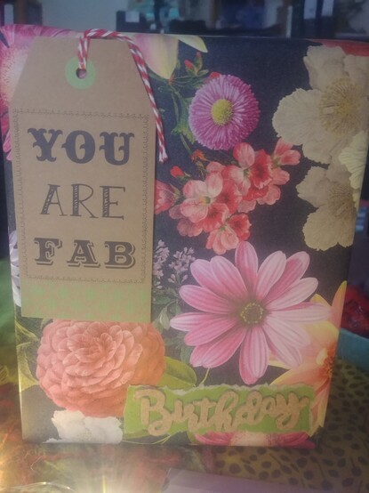 Ein in Blumnpapier verpacktes Geschenk.
Link oben hängt ein grosses Kraftpapier-Tag mit der Aufschrift you are fab.
Unten links ein usgerissenes grünes Stück Papier mit dem aus Kraftpapier ausgestanzten Schriftzug Birthday.