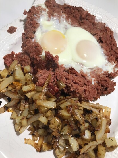Sunday breakfast on a white platter is corned beef hash, eggs, minced potatoes and onions.