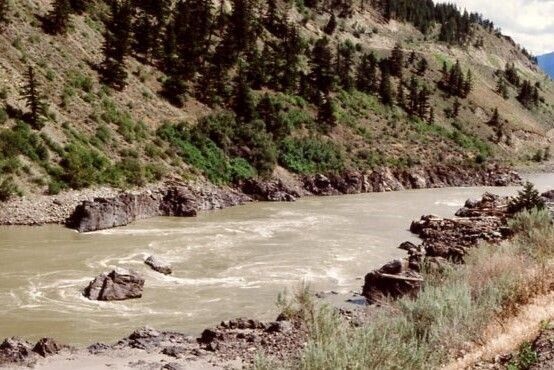 Rocks in the water of a fast moving river that flows through its rocky banks between high, bare hills. 