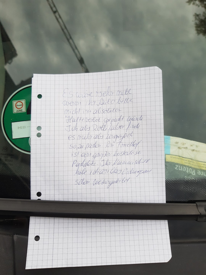 Handgeschriebener Zettel unter Scheibenwischer mit Text:
"Es wäre sehr nett wenn ihr Auto bitte nicht im absoliten Halteverbot geparkt würde.
Ich als Rollifahrer finde es mehr als unmöglich so zu parken. Am Friedhof ist ein großer kostenloser Parkplatz. Ihr Nummernschild habe ich an das Ordnungsamt schon weitergereicht."