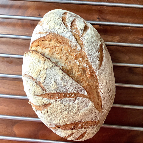 Baked bread with a design carved into it, on a grate on top of dark wood.