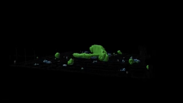 A neon green blob against a black background, surrounded by smaller bits of green and blue.