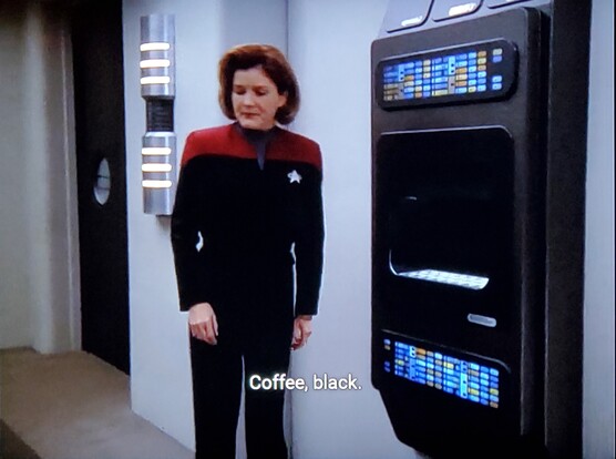 Voyager scene. Captain Janeway is standing next to a food replicator, which is wall panel with interface and a little cubby inside where things just appear when she asks for what she wants. It's an otherwise normal starship room, maybe a ready room or mess hall, hard to say. Ok so she's standing alongside it and the closed caption reads, "Coffee, black."
Next picture is closer in and Janeway looks surprised and taken aback looking at the replicator. Closed caption reads, "[Computer]: Make it yourself."