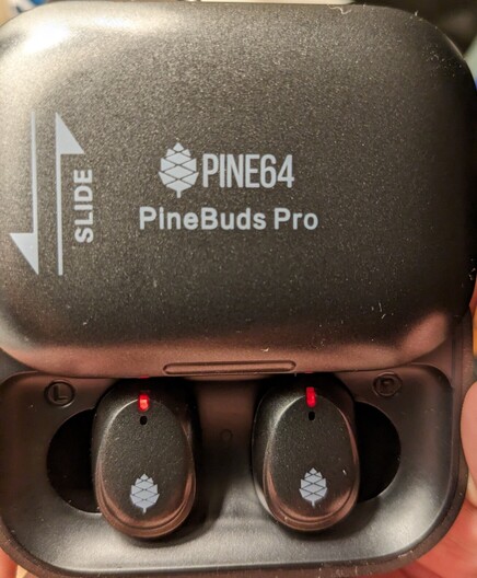 A pair of Pine buds Pro in their charging case. The case is slid open to reveal the ear buds inside.
