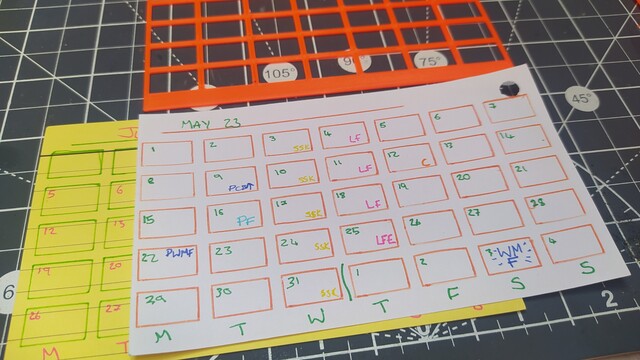 Photo of a orange 3d printed stencil above an index card converted into a calendar. 
