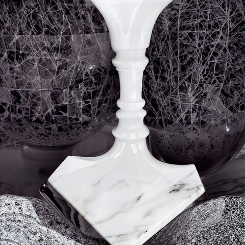 A black and white photo of a white marble column with a dark background featuring a network of straight lines. Or is it the dark silhouette of two profiles looking at each other on a white background in the centre?