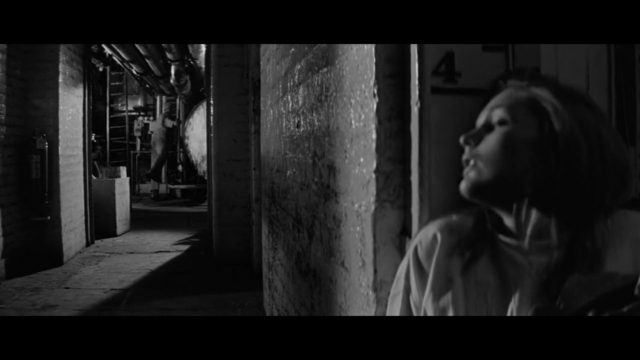 In a boiler room, a woman pressed herself against a wall in fear.