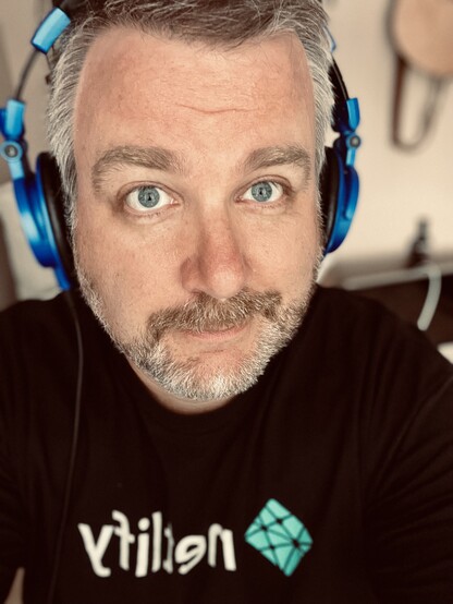 selfie of me with a pair of blue headphones on looking into the camera with eyes that aren't dilated. i have a beard? i don't know how else to describe myself.