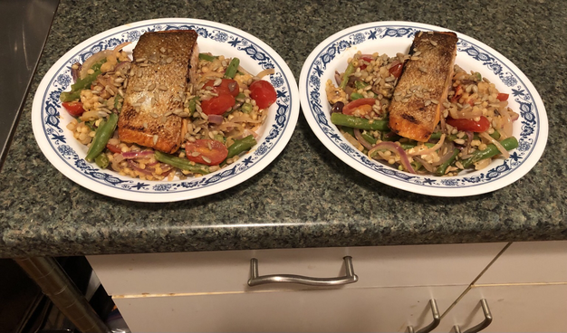 Plated dish. Pan seared trout on a bed of pearl couscous, green beans, grape tomatoes, niçoise olives, and feta that was baked together. Garnished with sunflower seeds.