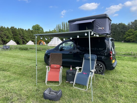 A Citroen Berlingo van with awning, tentbox, camping gear in a camping field.