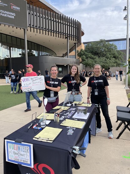 Volunteers outside of Moody Center, holding up a whiteboard where people vote on their favorite The Cure song 