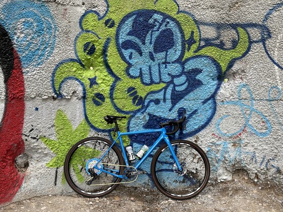 A blue gravel bike against a graffiti wall