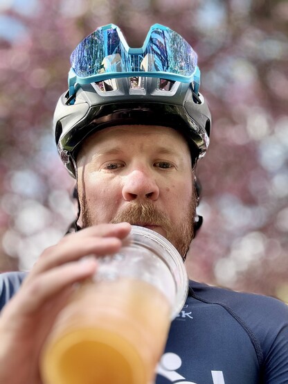 A cyclist drinking a mango iced drink with cherry blossoms in the background, blurred
