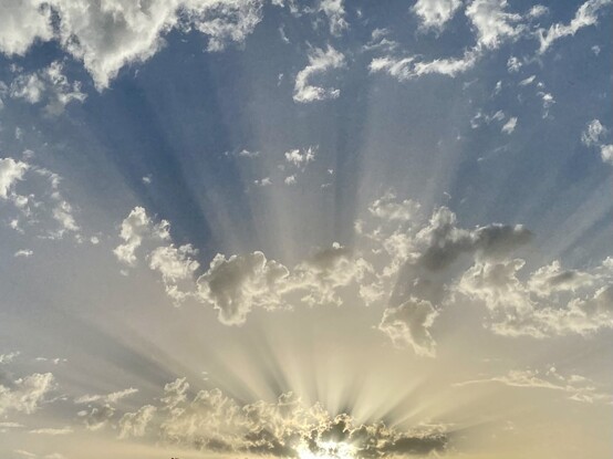 Sunbeams and clouds at sunset. The sky is pale yellow near the horizon and grey blue beyond. 