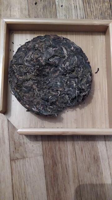 A puerh cake (compressed tea leaves) on a too big puerh tray (a small squarish tray with a corner without border to make it easier to pour the leaves)