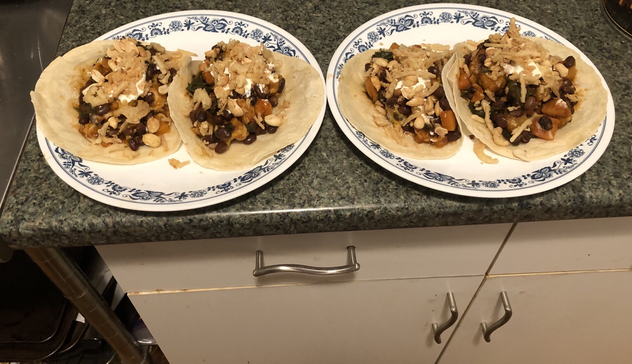Plated dish. 2 flour tortillas filled with black beans, butternut squash, spinach, melted cheddar and Monterey Jack cheese. Topped with sour cream and crispy onions.