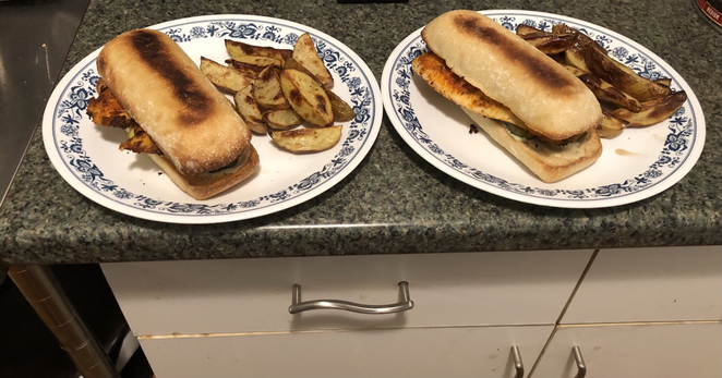 Plated dish. The build: Bottom roll, slather of Dijon and mayo, garlic dill pickle chips, Cajun seasoned tilapia, top roll. Roasted potato wedges. Not pictured: Spicy ketchup.