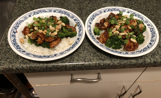 Plated dish. Chicken and broccoli tossed in a spicy sauce on top of rice. Garnished with scallions and peanuts.